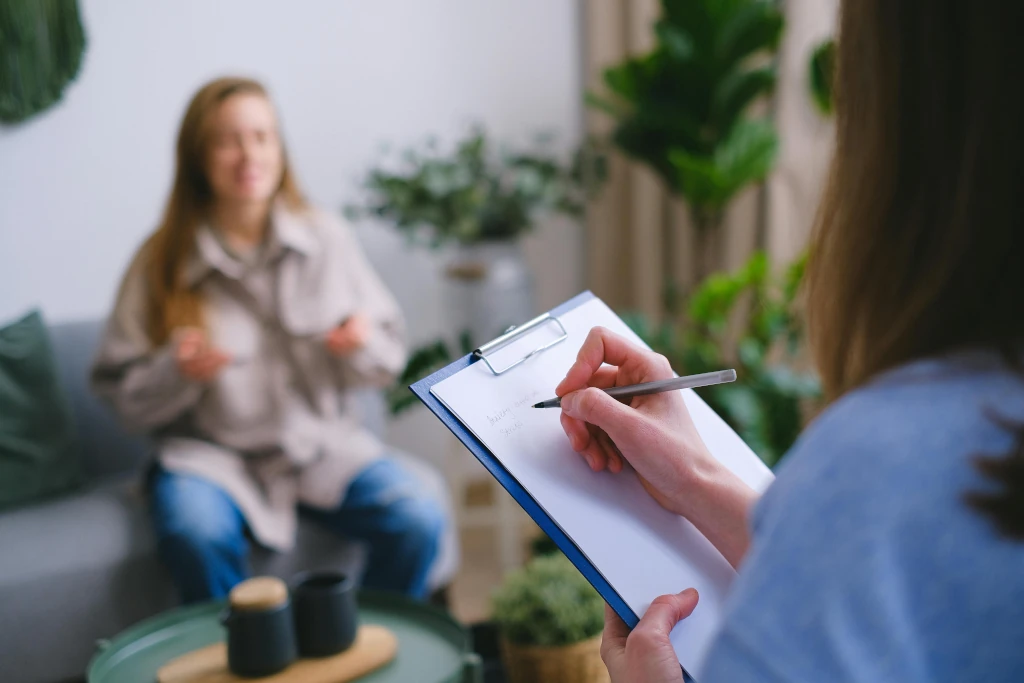 Frau mit Clipboard macht Notizen während sie sich mit einer anderen Frau unterhält. 